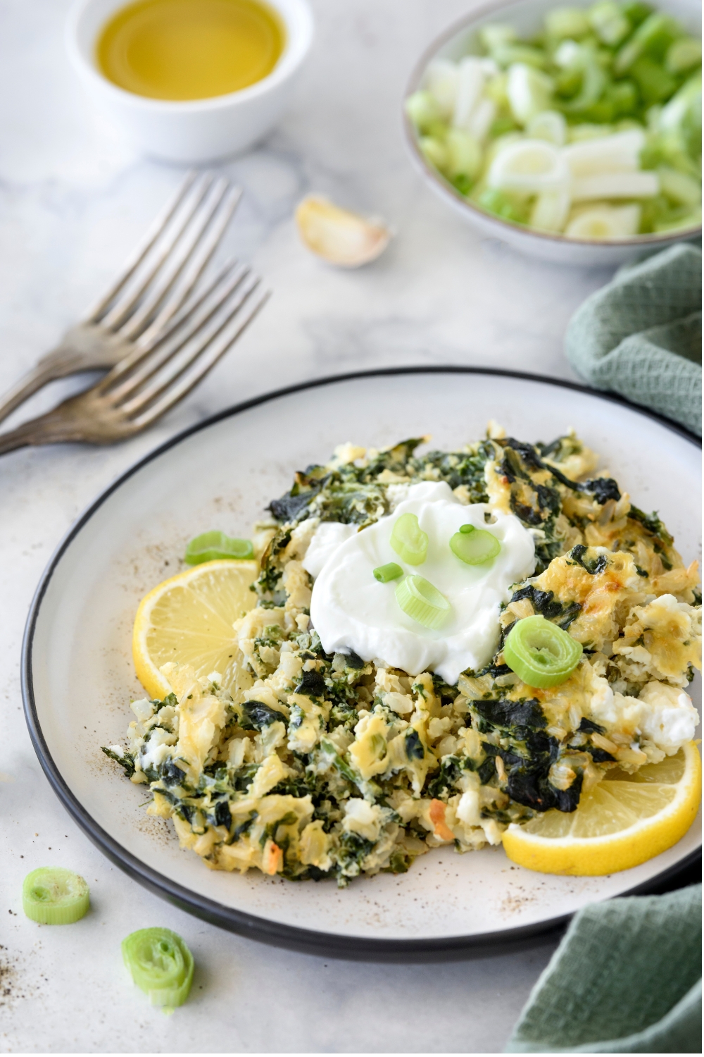 A plate with spinach rice casserole garnished with a dollop of yogurt, green onions, and a lemon wedge.