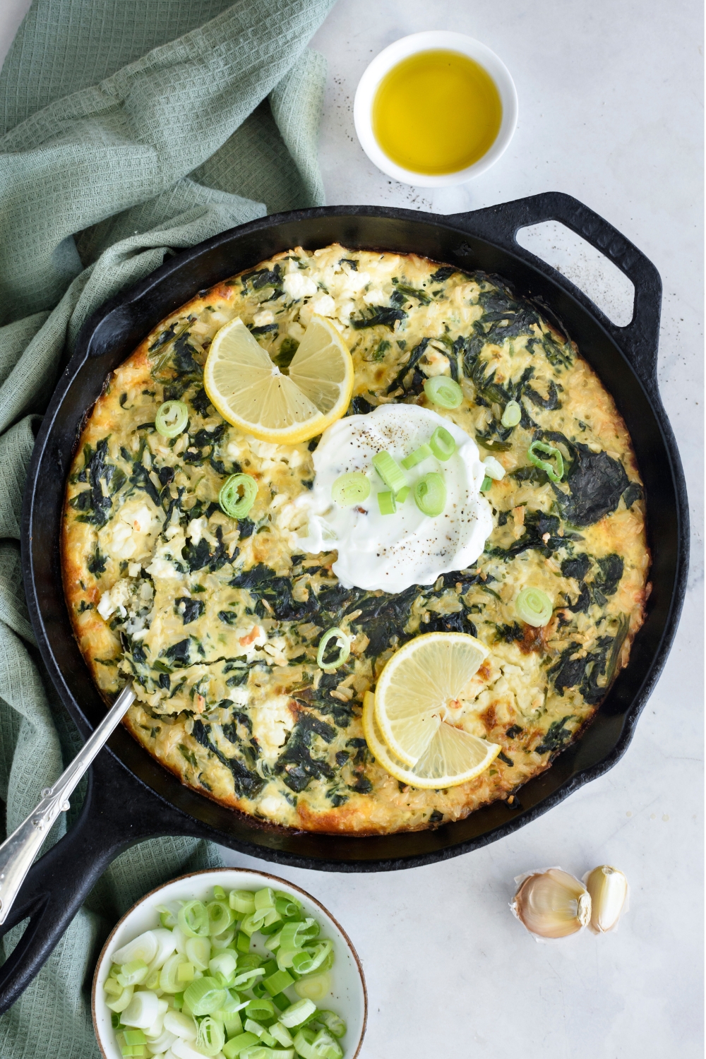 A skillet with spinach rice casserole with a dollop of yogurt, green onions, and lemon wedges.