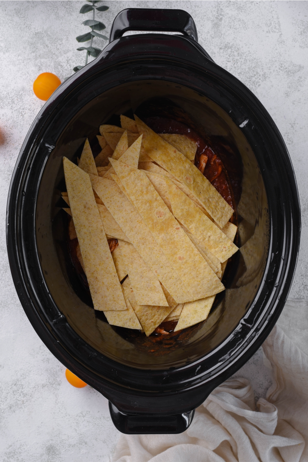 A crockpot with corn tortillas added to the enchilada shredded chicken.