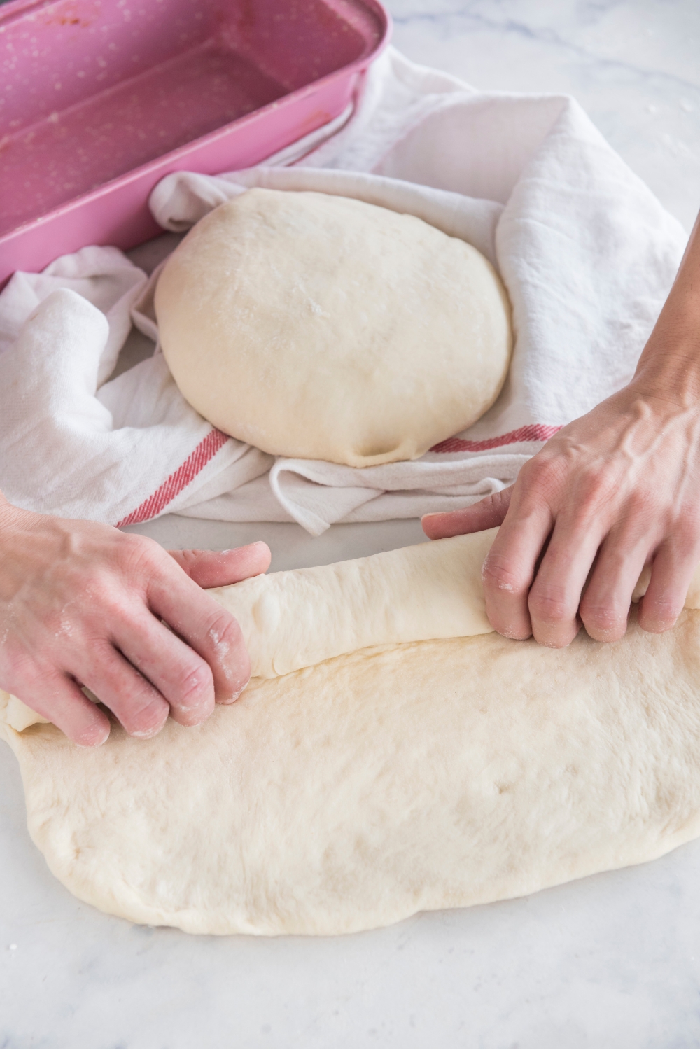 Flattened dough being wrapped into a tube/loaf shape.