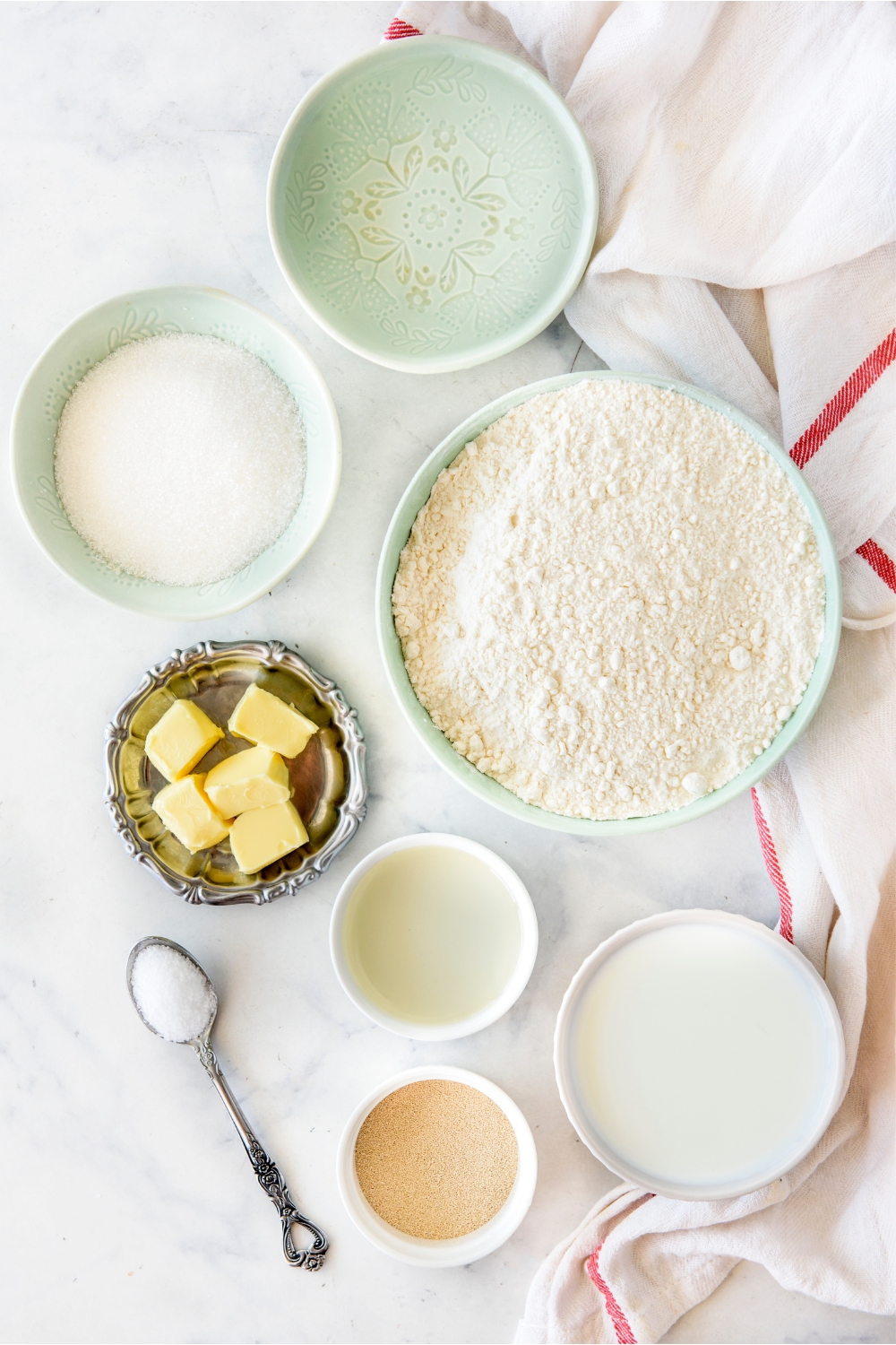A countertop with flour, warm water, sugar, butter, milk, yeast, salt, and oil in various bowls.