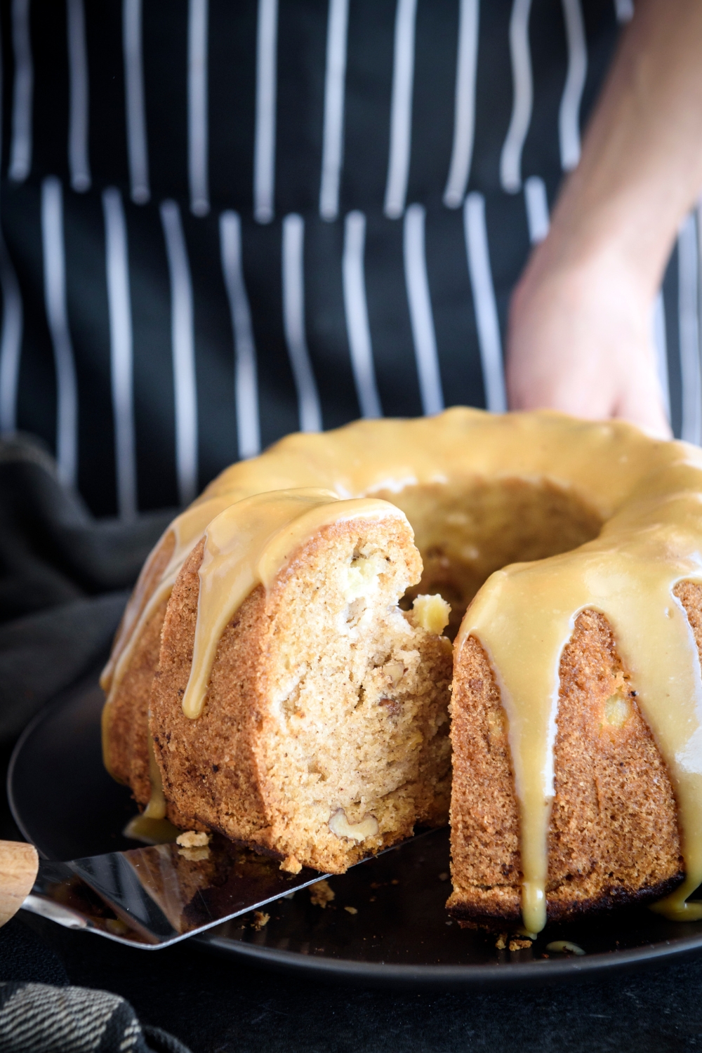 A bundt cake covered in a caramel glaze with a slice being removed.