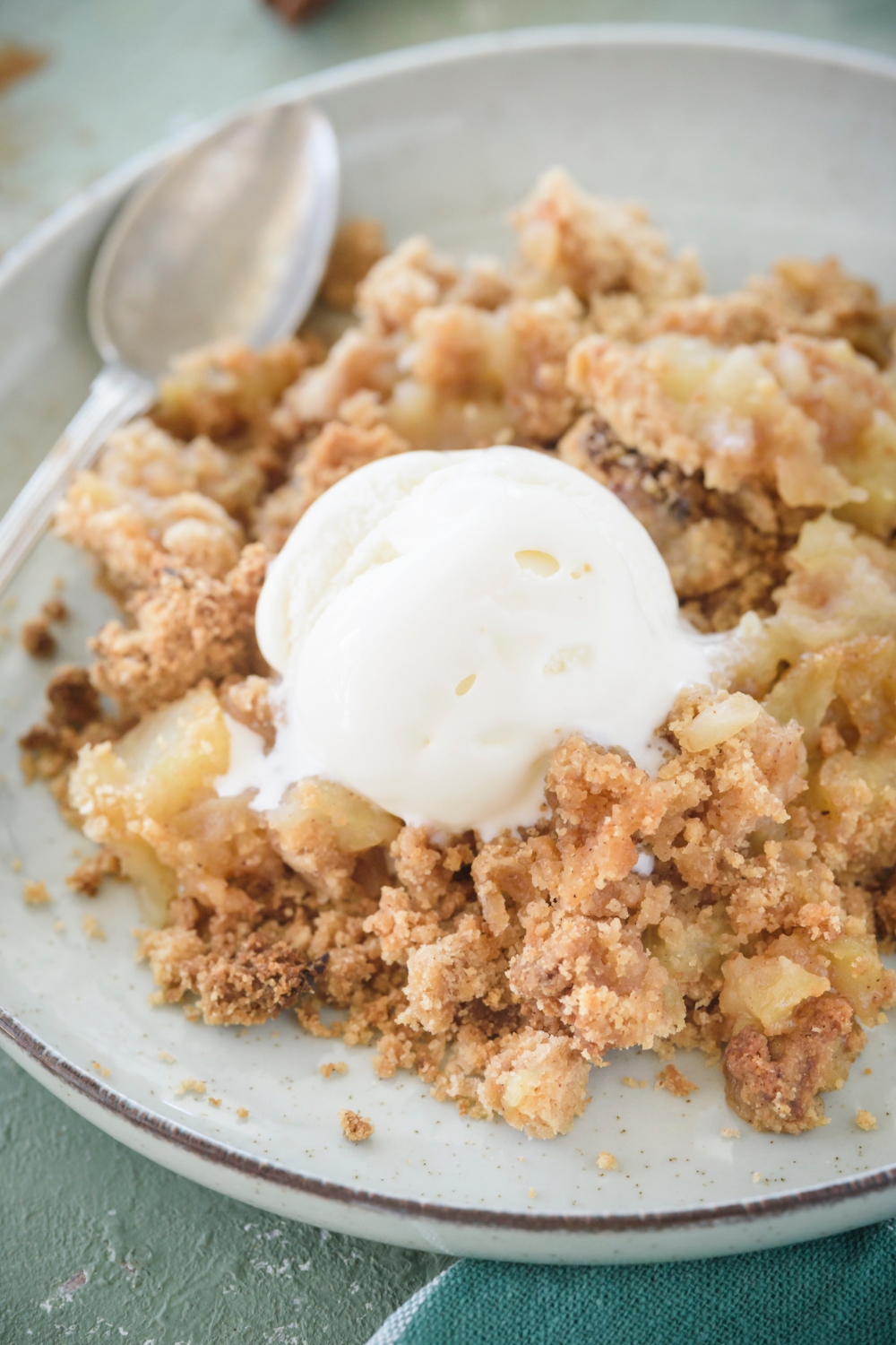 Apple crumble on a plate with a scoop of ice vanilla ice cream on top. The ice cream is melting into the crumble and a spoon is on the plate.