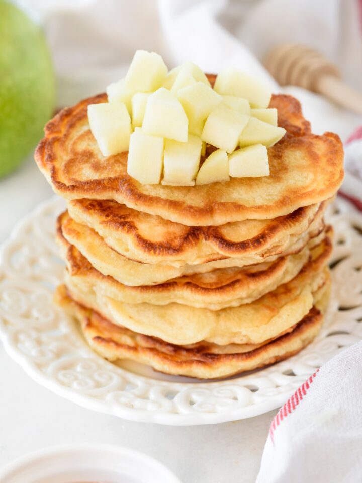 A tall stack of golden brown pancakes topped with diced apples.