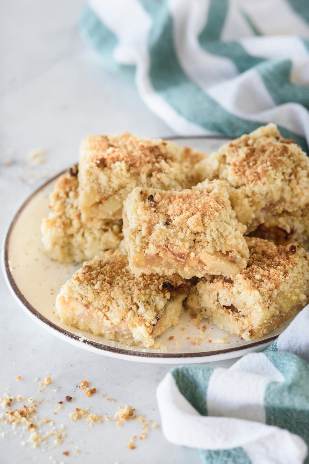 Apple pie bars piled high on a plate topped with a crumbly golden brown topping.