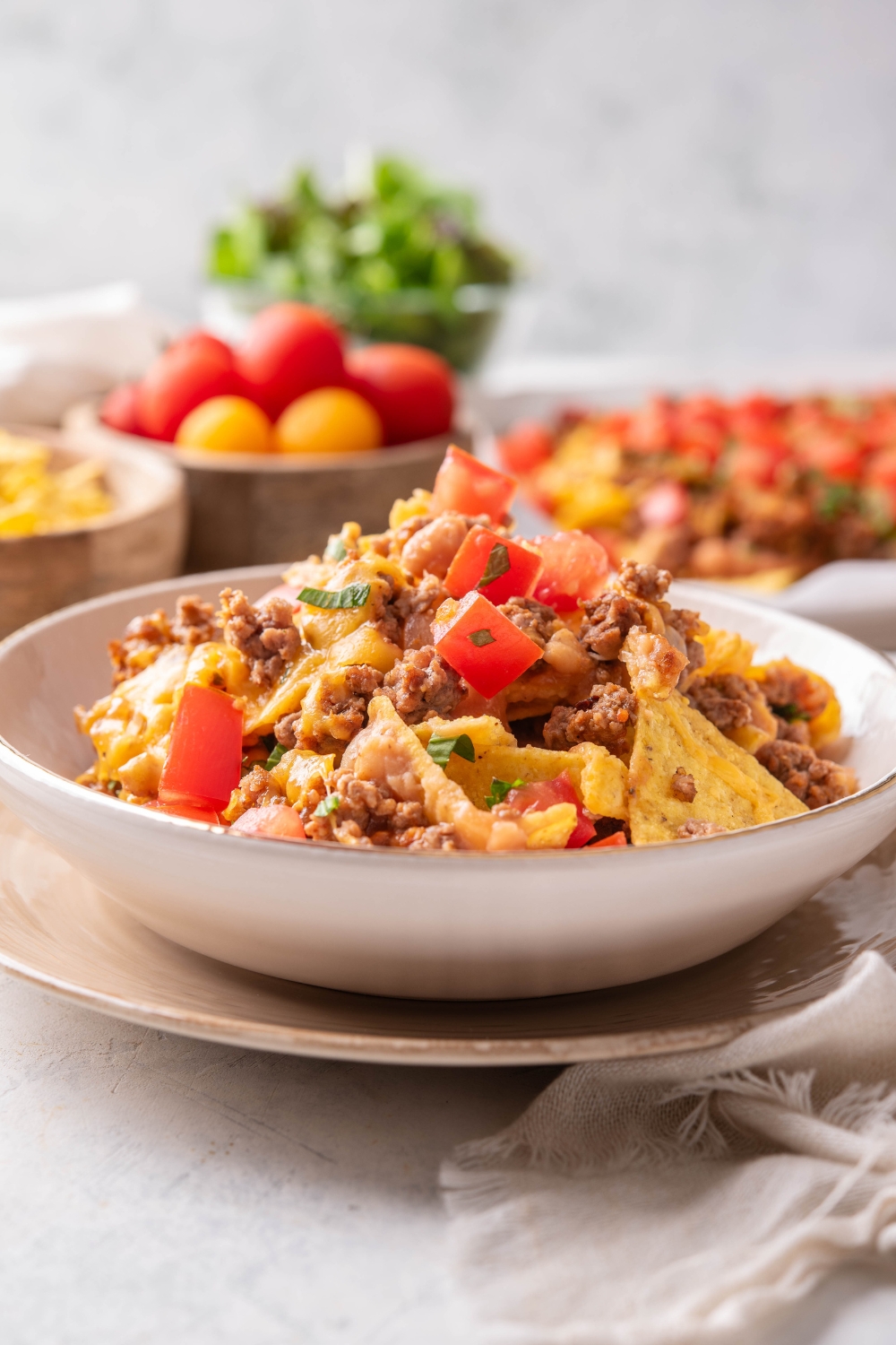 A bowl of beef nachos topped with diced tomatoes, beef, melted cheese, and cilantro.