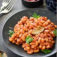 a black plate with cooked baked beans on it with two forks.