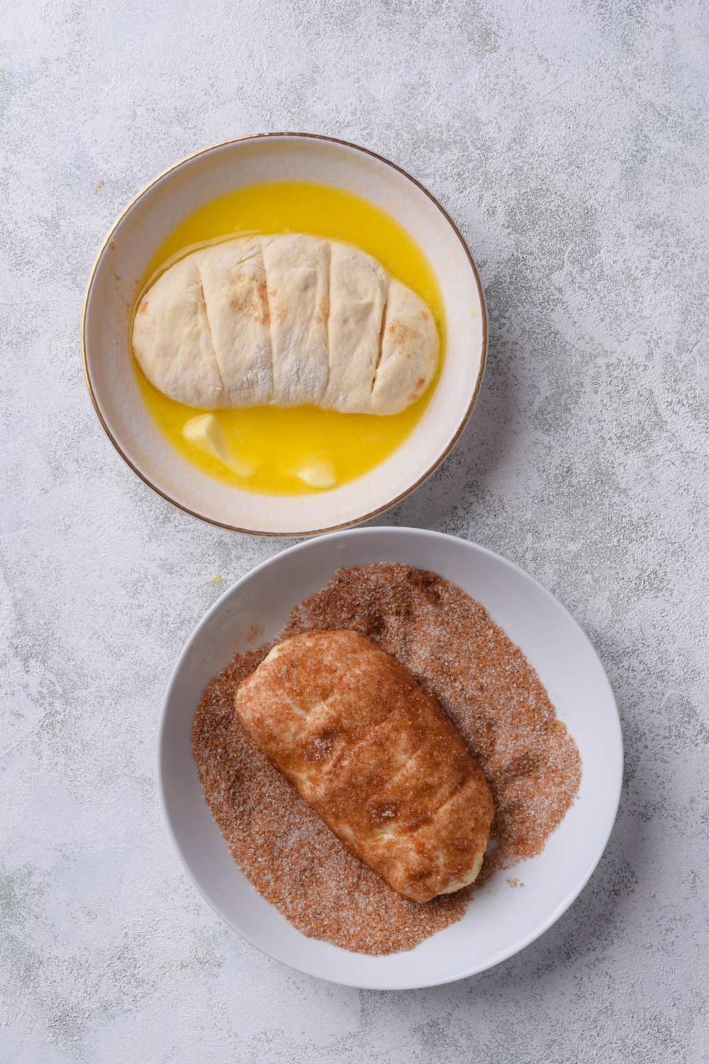 a raw loaf of dough in a bowl of butter next to a raw loaf of dough in a bowl of cinnamon and sugar