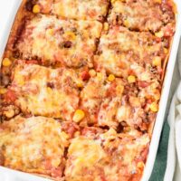 A baking dish filled with freshly baked casserole covered in melted cheese and cut into eight equal-sized pieces.