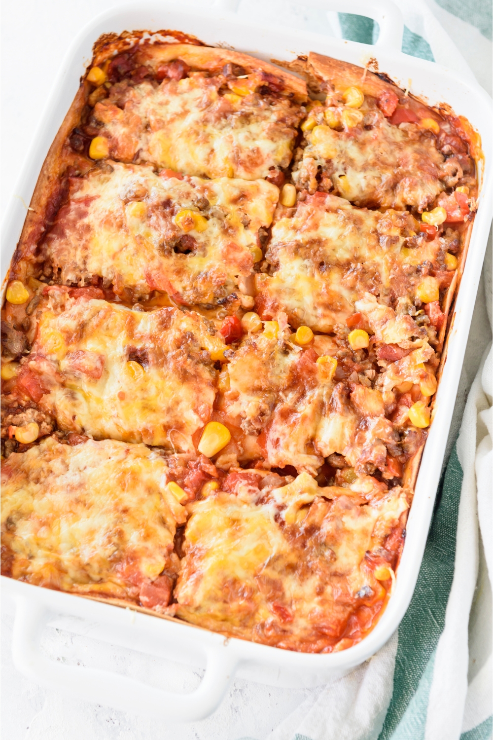 A baking dish filled with freshly baked casserole covered in melted cheese and cut into eight equal-sized pieces.