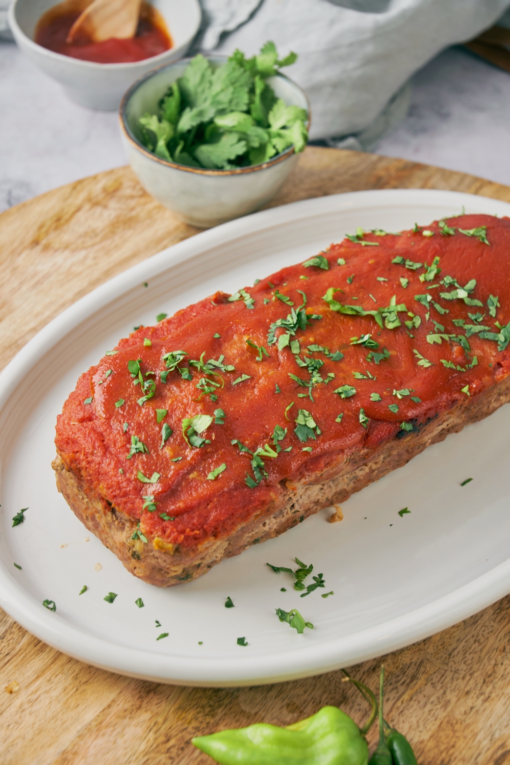 Meatloaf on a white plate covered in red sauce and garnished with fresh green herbs.