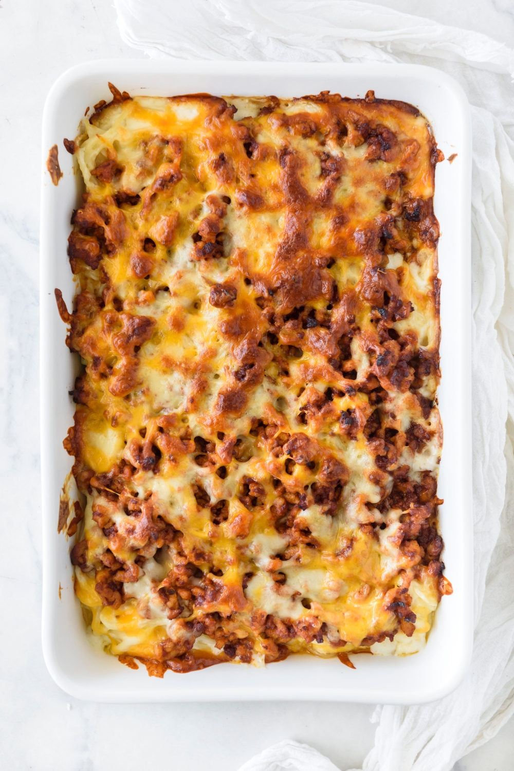 A baking dish filled with baked spaghetti covered in melted cheese with chunks of cooked ground meat.