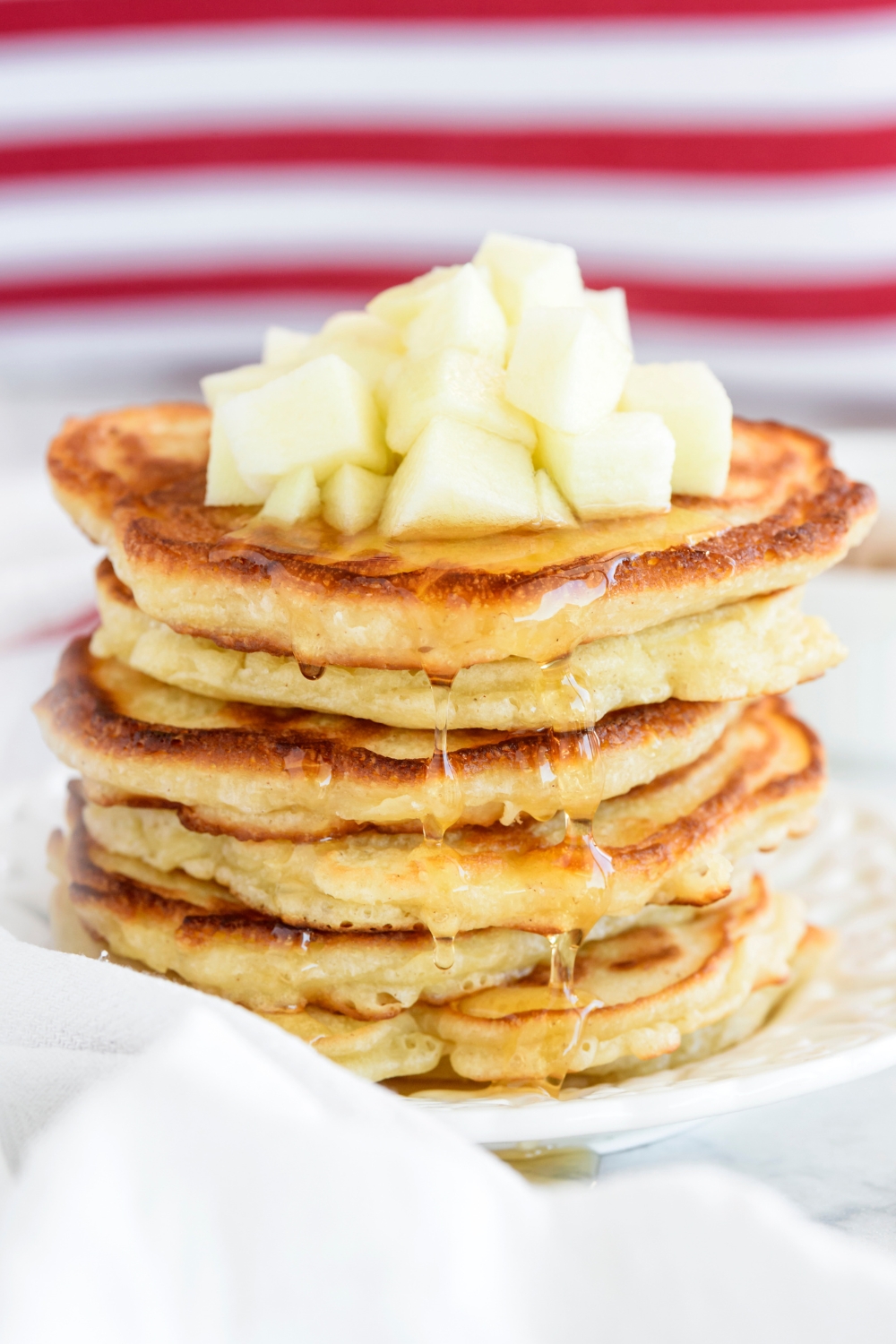 A stack of golden brown pancakes topped with diced apples with honey dripping down the sides of the pancakes.