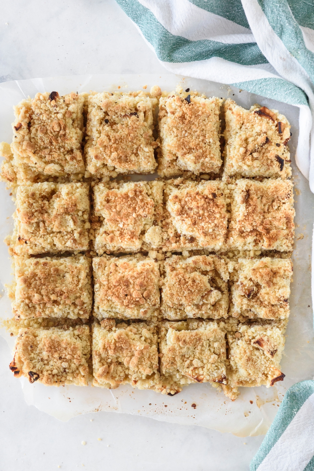 Apple pie bars cut into sixteen equal-sized squares on a sheet of parchment paper.