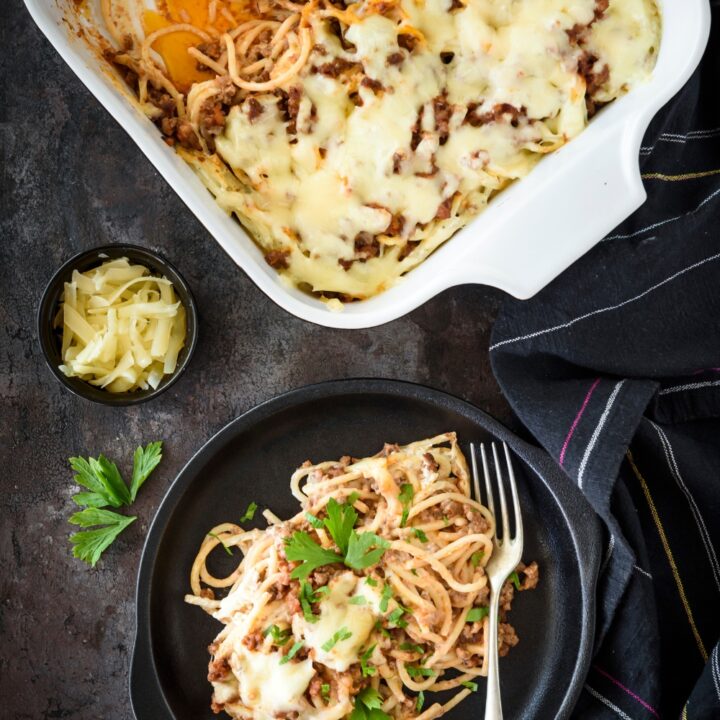 A bowl of spaghetti topped with fresh herbs and melted cheese next to a casserole dish filled with more spaghetti.