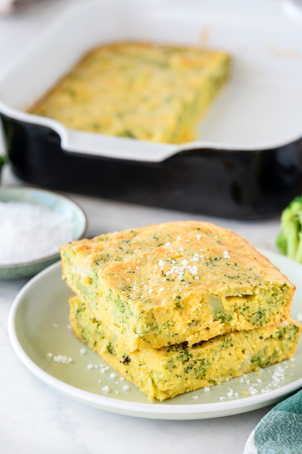 Two squares of broccoli cornbread stacked on top of each other garnished with sea salt.