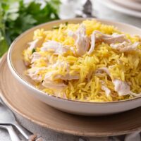 A bowl filled with yellow rice and cooked shredded chicken mixed together beside a set of silverware.