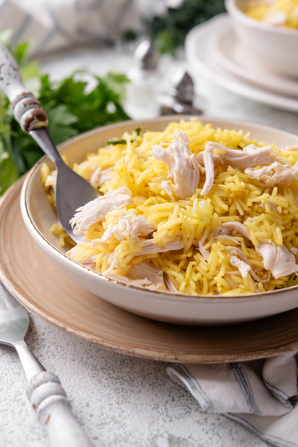 A bowl of yellow rice and shredded chicken mixed together and a fork is grabbing a scoop of rice and chicken from the bowl.