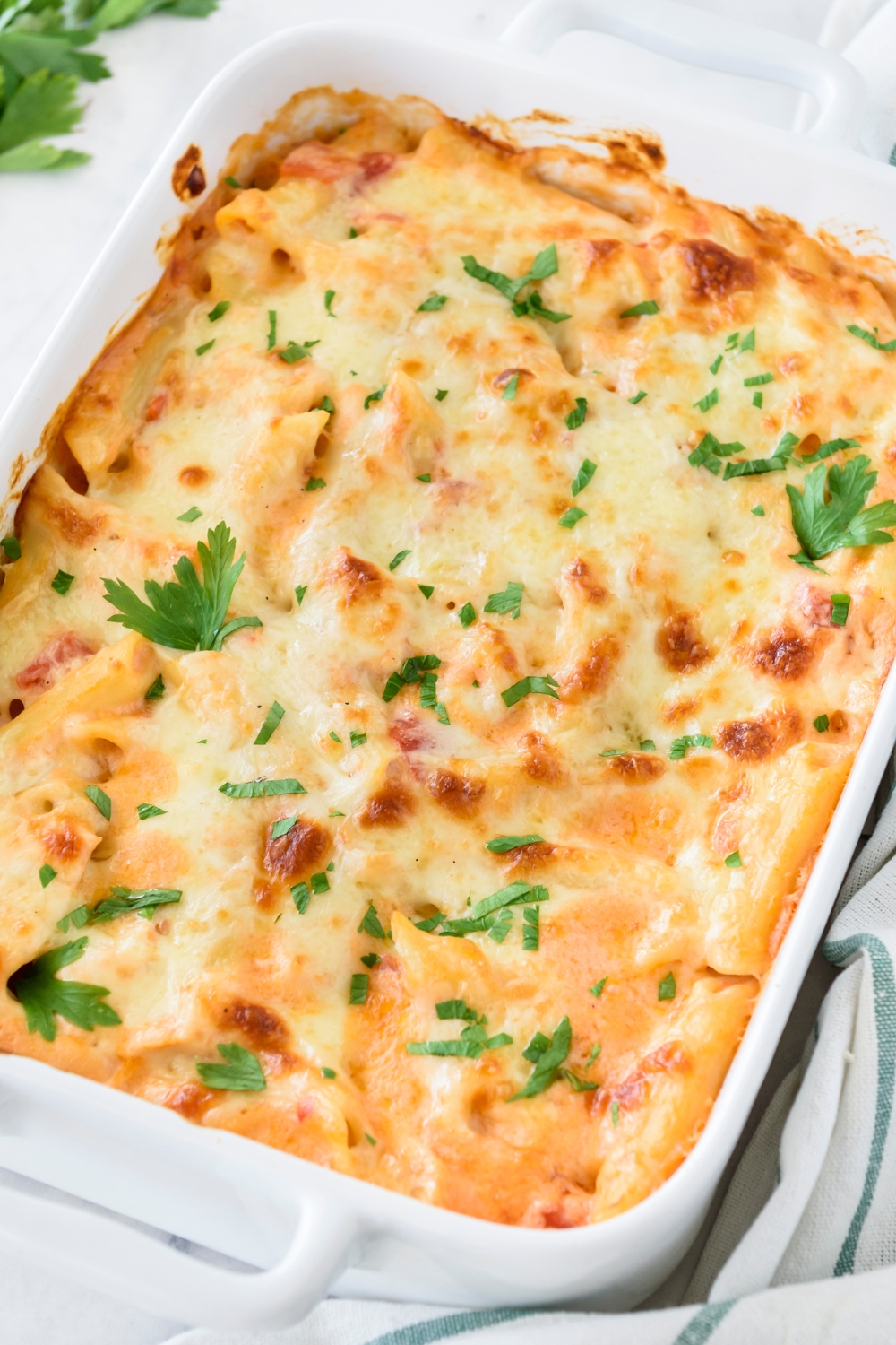 A baking dish filled with freshly baked casserole covered in melted cheese and fresh green herbs.