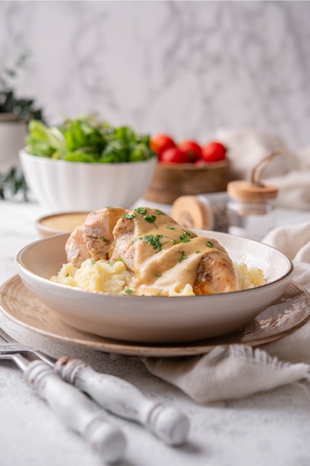 A plate of cooked and sliced chicken breast covered in a creamy brown sauce, garnished with fresh herbs, on a bed of mashed potatoes.