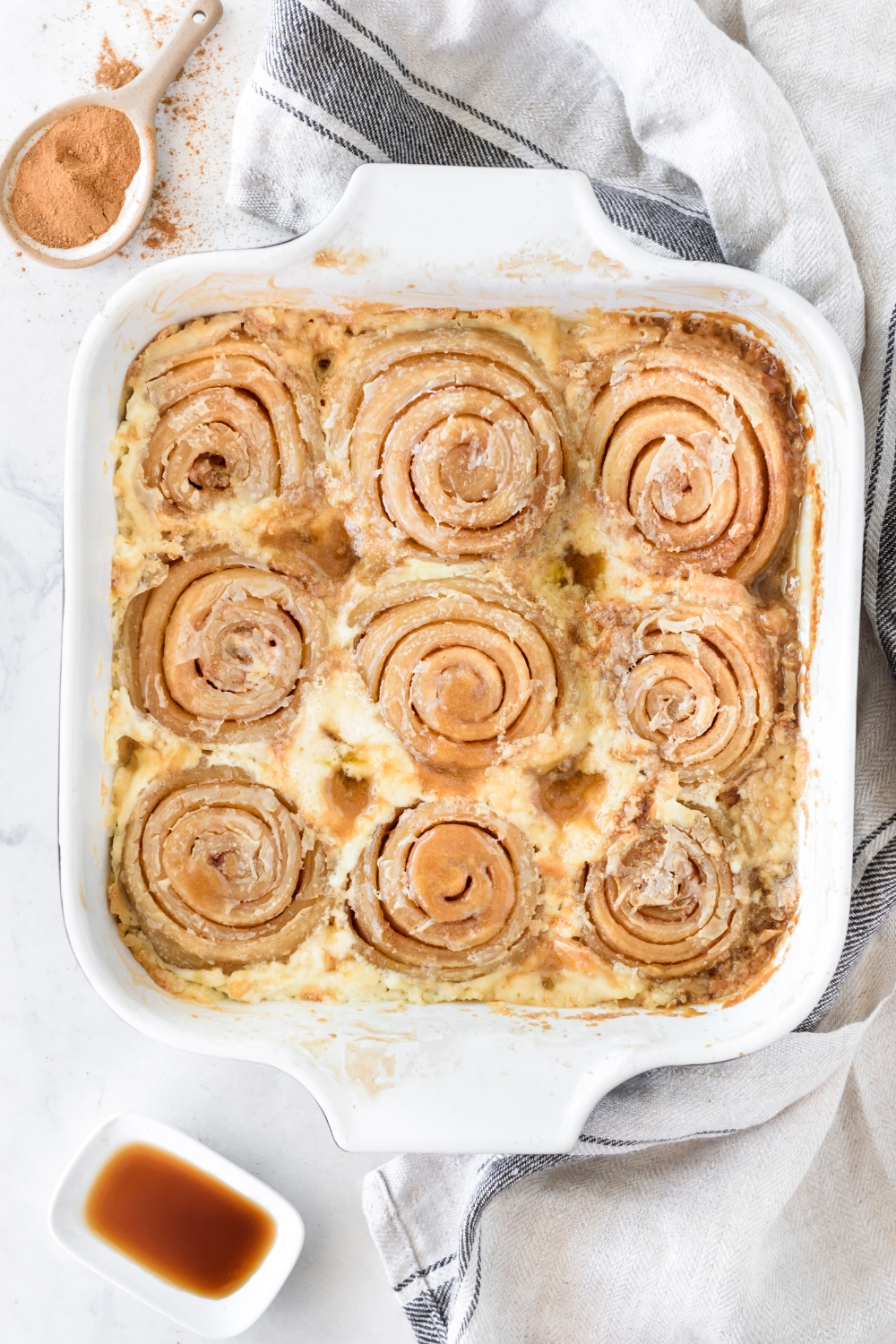 A baking dish filled with freshly baked cinnamon rolls covered in a cream.