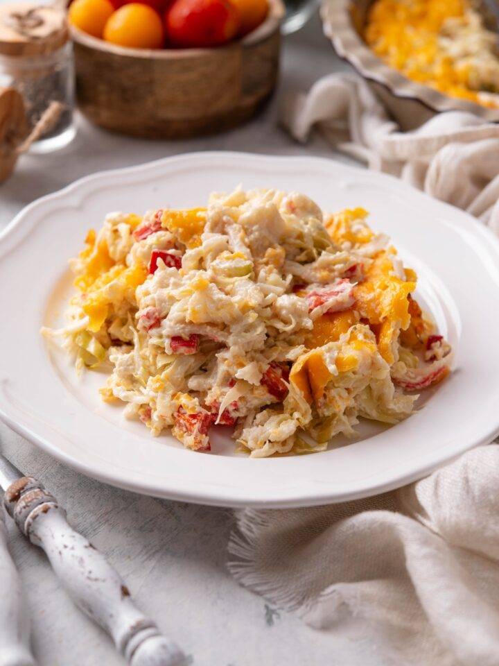 A plate of creamy crab casserole with melted cheese, diced red peppers, and sliced cabbage.