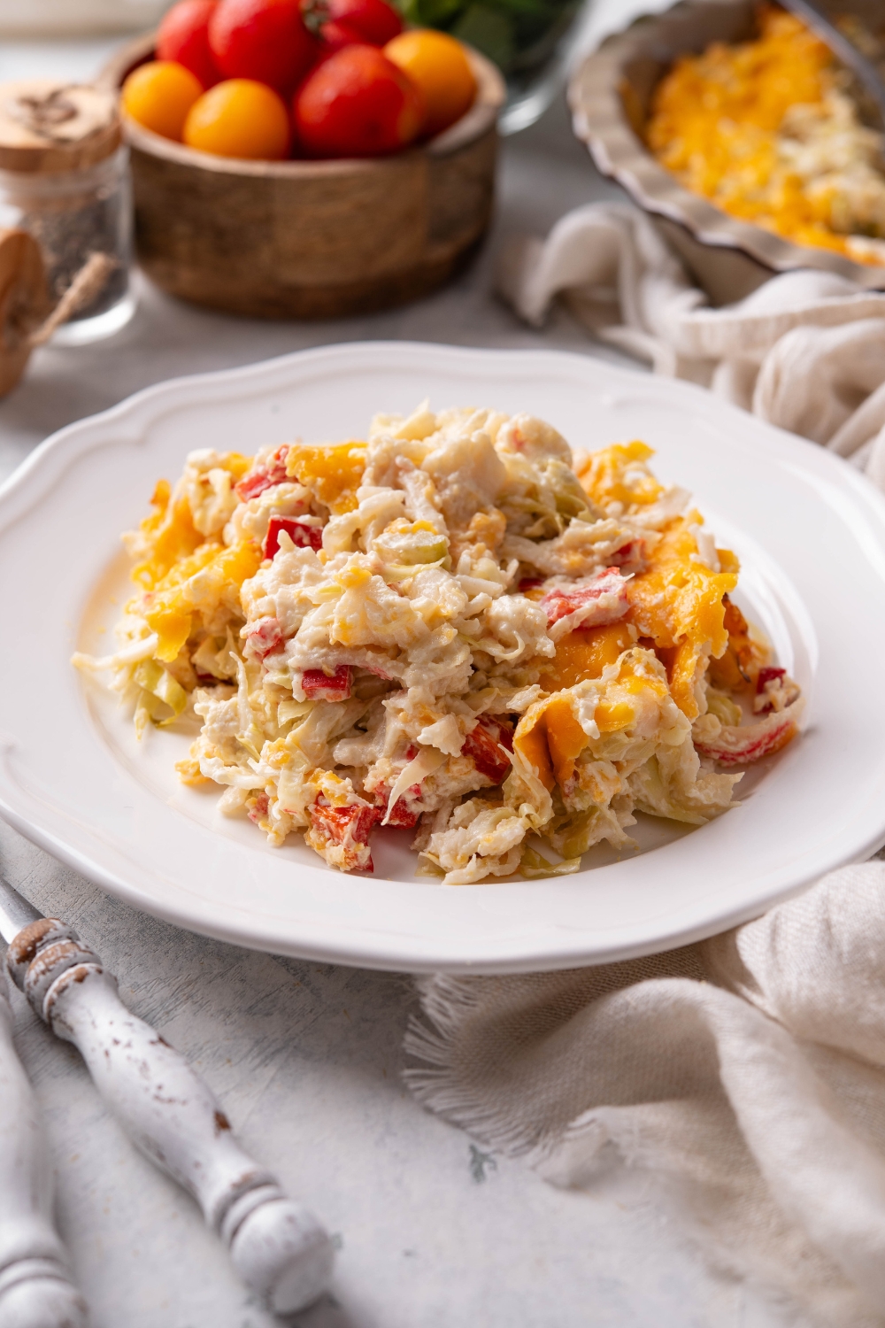 A plate of creamy crab casserole with melted cheese, diced red peppers, and sliced cabbage.