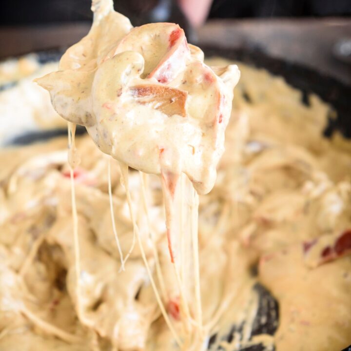 A spoonful of creamy chicken and vegetables with cheese stringing from the spoon to the skillet below.