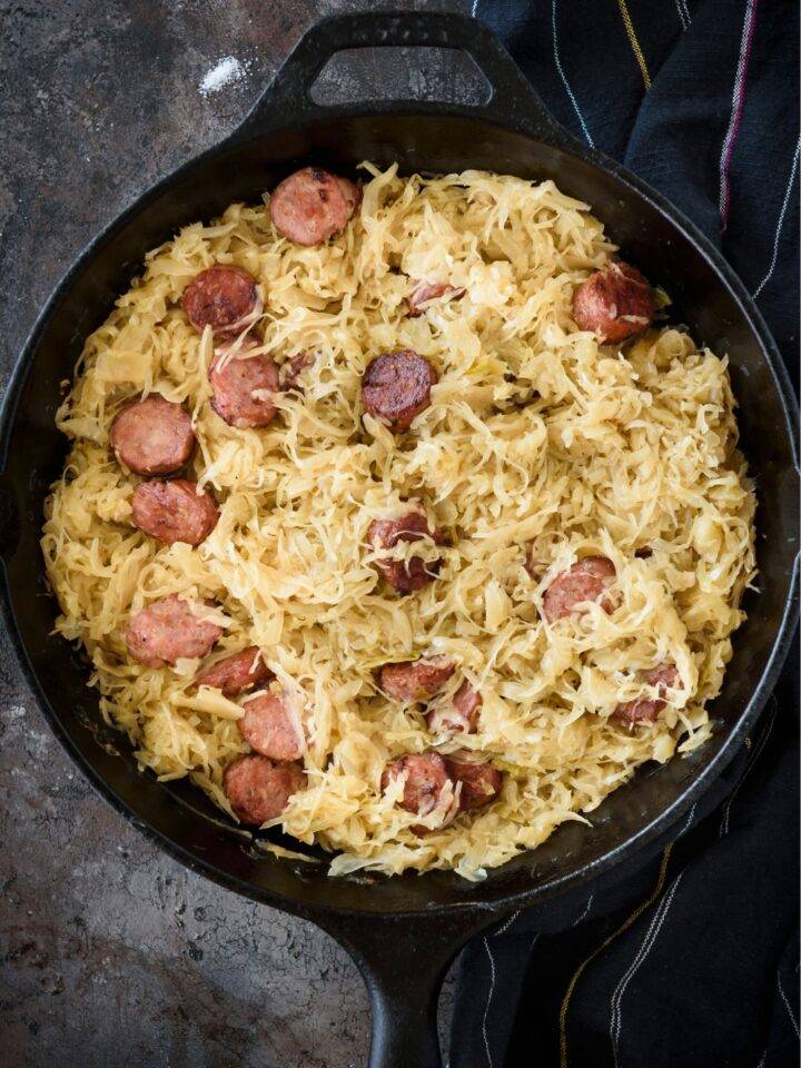 A cast iron skillet filled with sauerkraut and sliced sausages.
