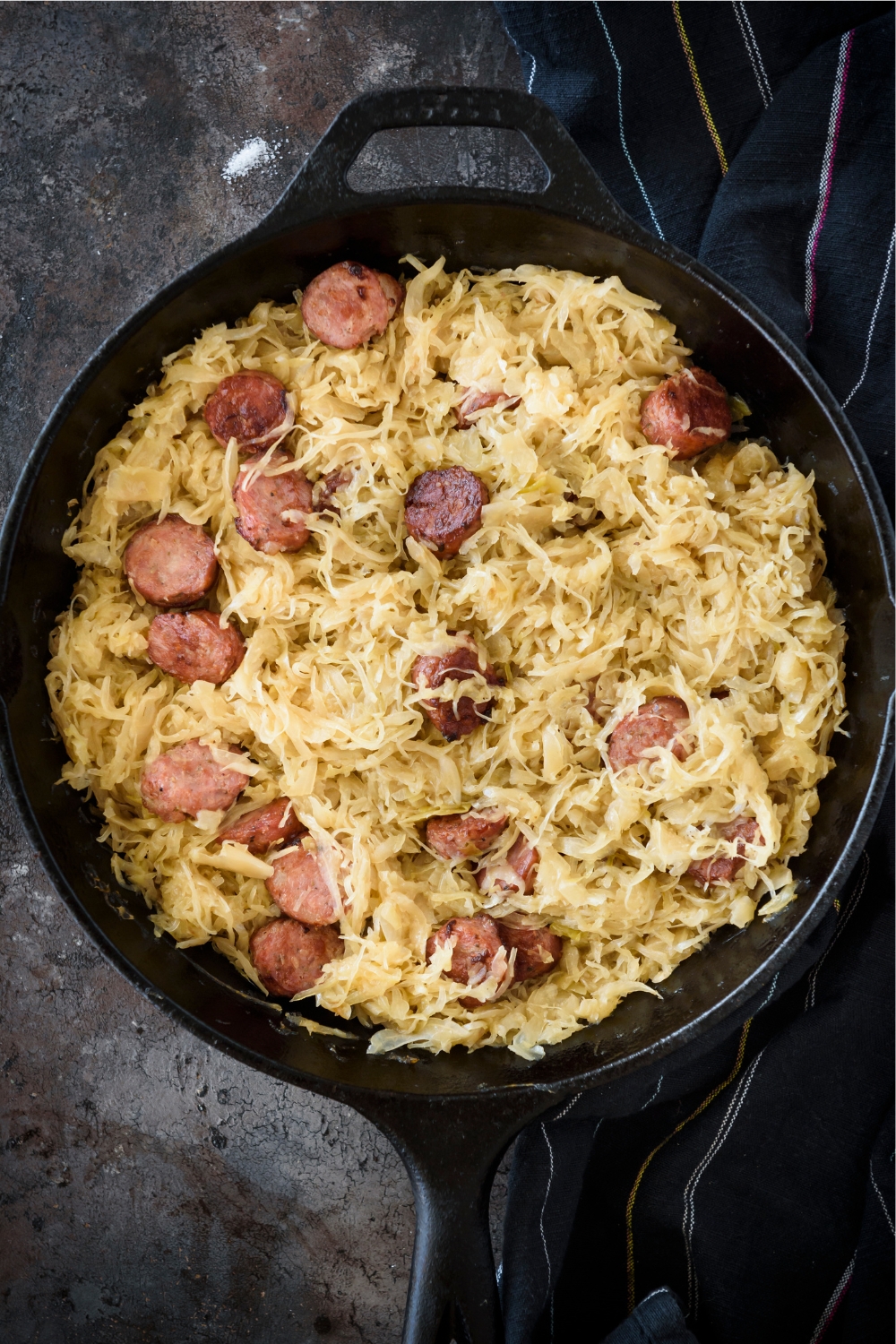 A cast iron skillet filled with sauerkraut and sliced sausages.