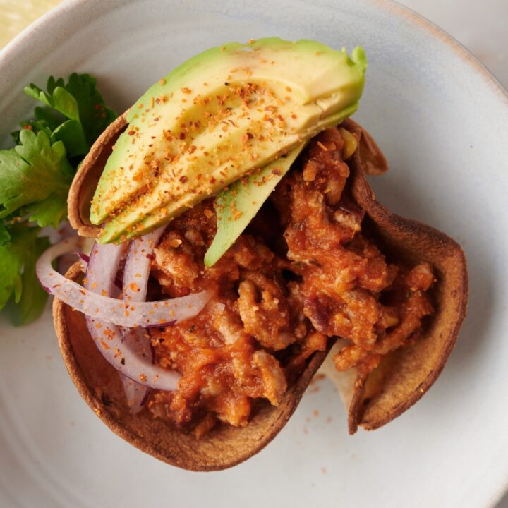 Mexican chili served with avocado and onion on a white plate