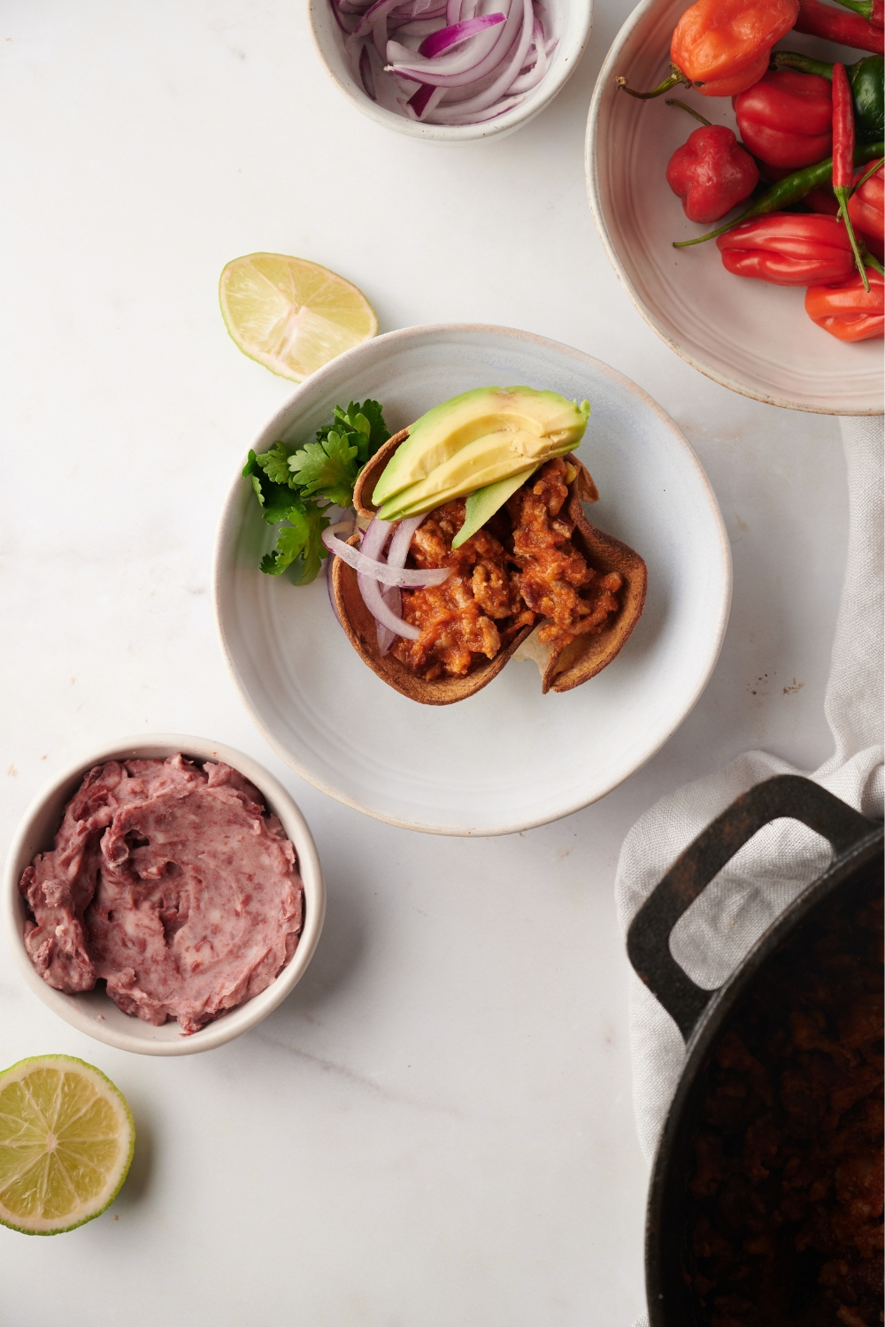 Completed Mexican chili served in a tortilla bowl on a white counter with avocado and onion