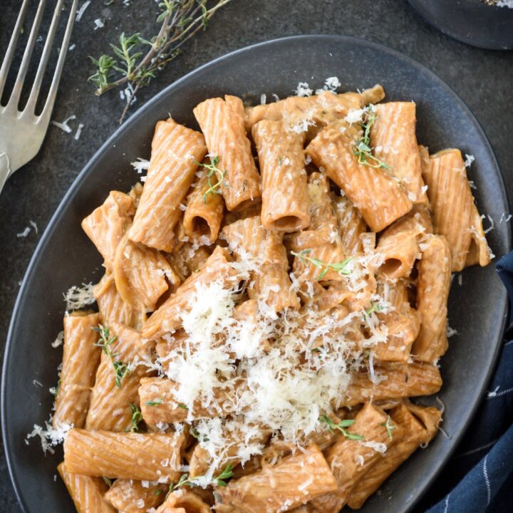 A plate of rigatoni pasta covered in a brown cream sauce and topped with fresh herbs and grated cheese.