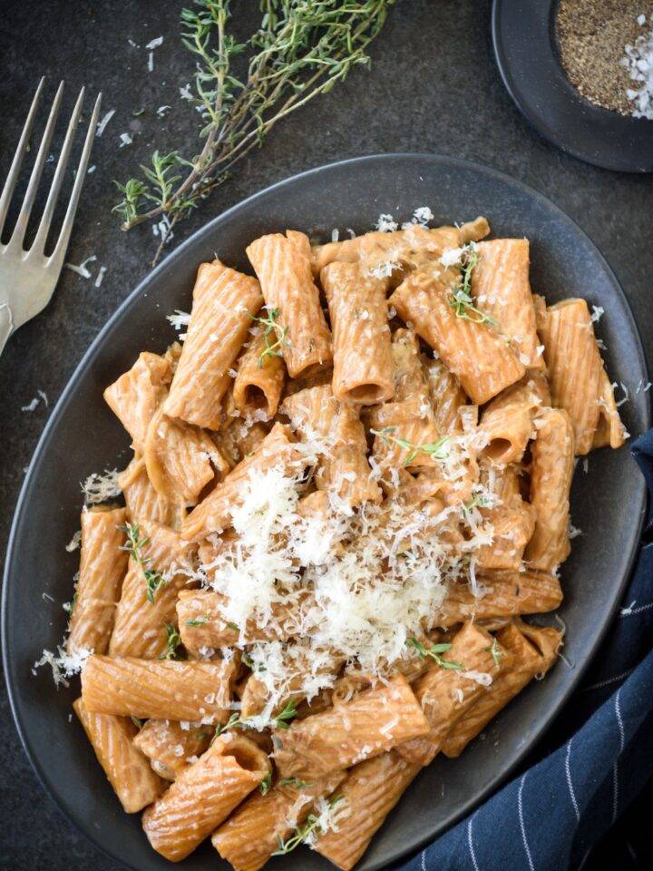 A plate of rigatoni pasta covered in a brown cream sauce and topped with fresh herbs and grated cheese.