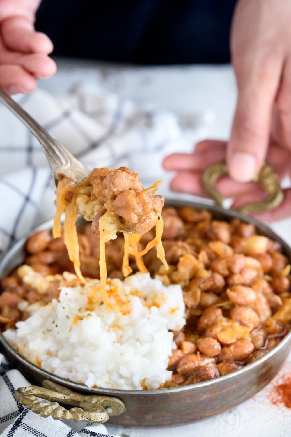 A forkful of cooked pinto beans with pieces of cooked onion held above a bowl of beans and white rice.