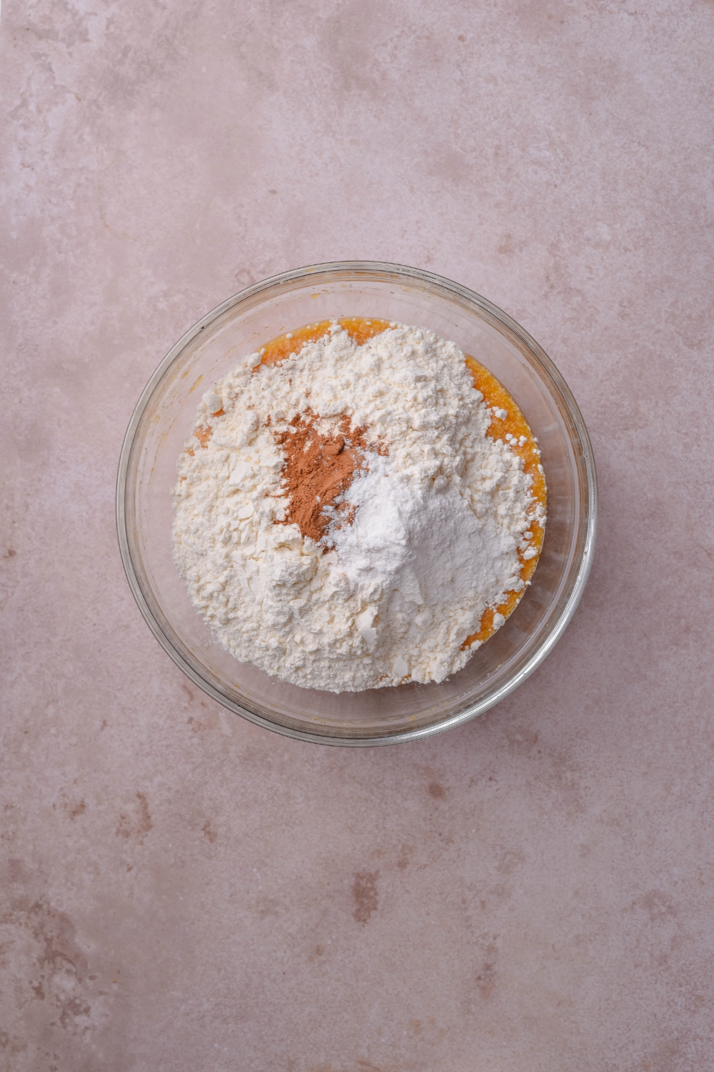 A clear bowl filled with flour, baking powder, and spices.