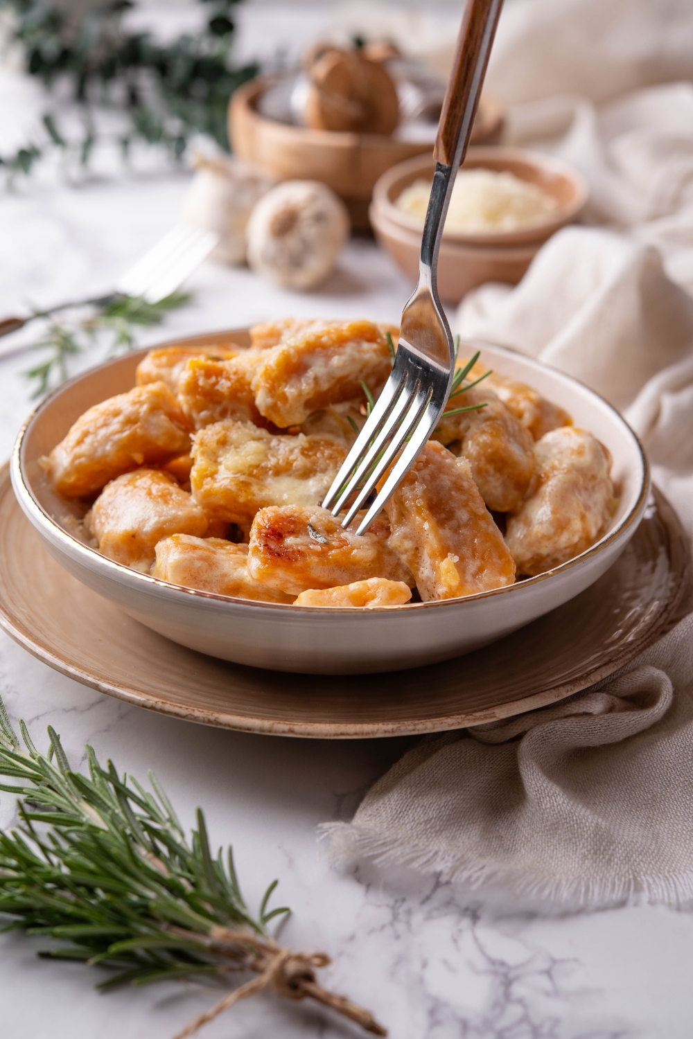 A bowl of sweet potato gnocchi covered in cream sauce with a fork taking a piece of gnocchi out of the plate.