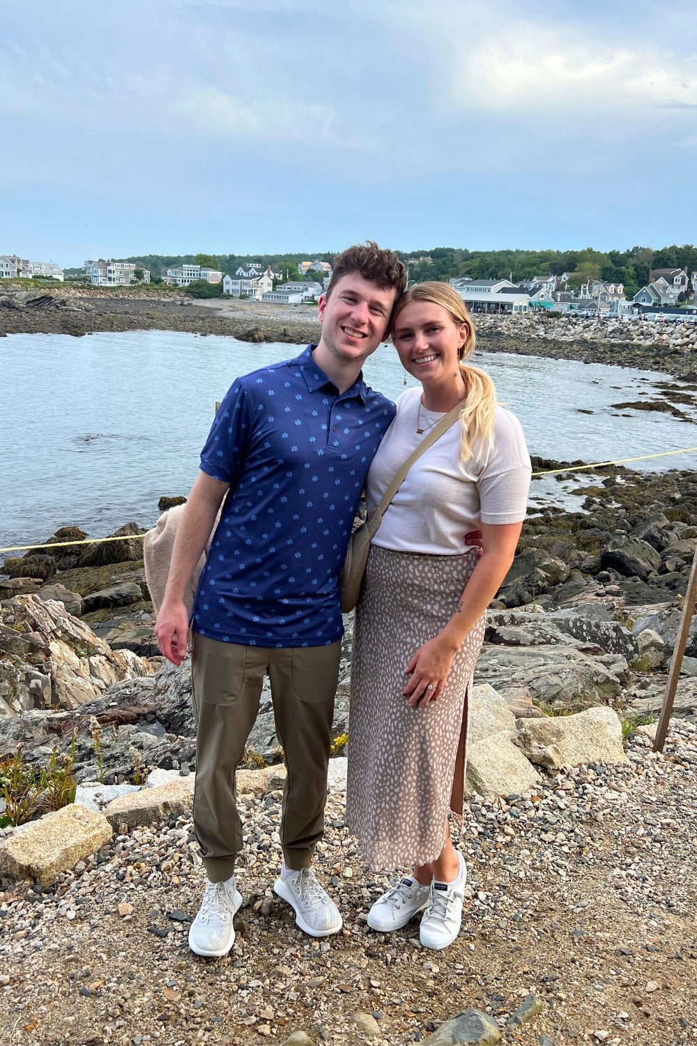 A man and a woman standing in front of rocks in front of a bay of water.