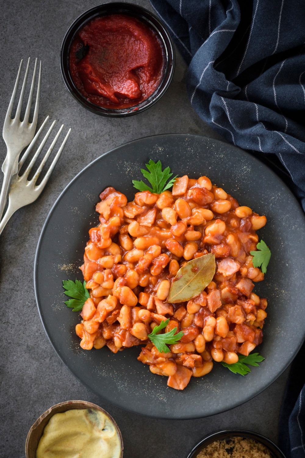 A black plate with cooked baked beans on it.