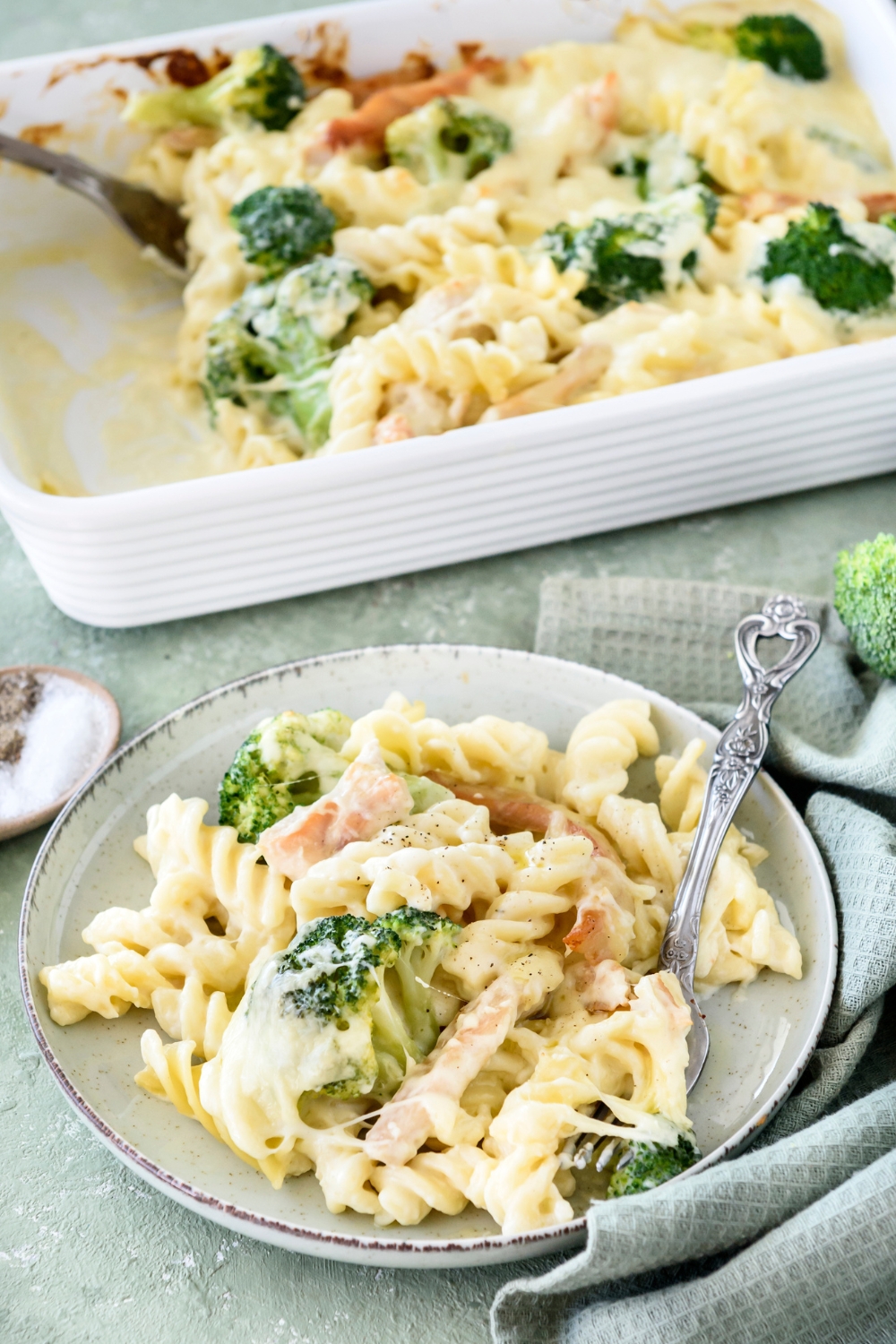 A bowl of pasta in cream sauce with chicken strips and cooked broccoli mixed in the pasta. The rest of the pasta is in a casserole dish in the background.