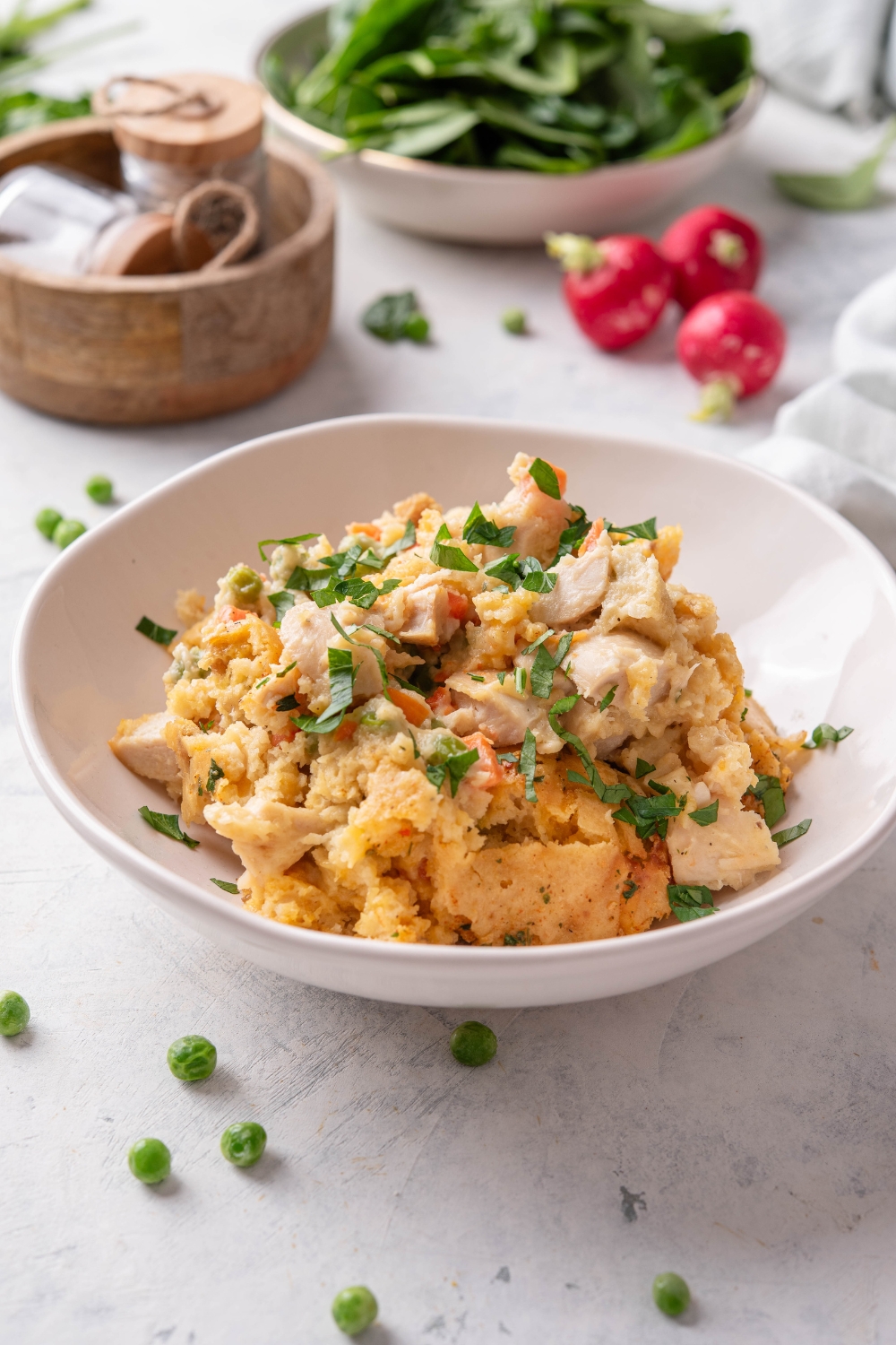 A bowl of chicken casserole with cooked chicken in a creamy sauce mixed with carrots, peas, and a crumbly biscuit topping and garnished with fresh herbs.