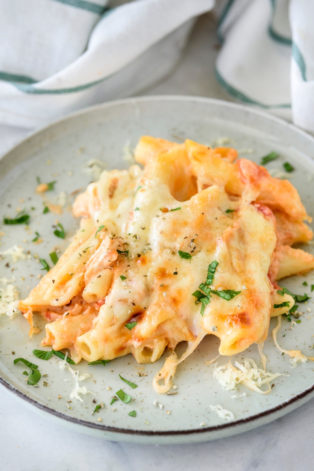 A plate of chicken pasta bake covered in melted cheese and fresh green herbs.