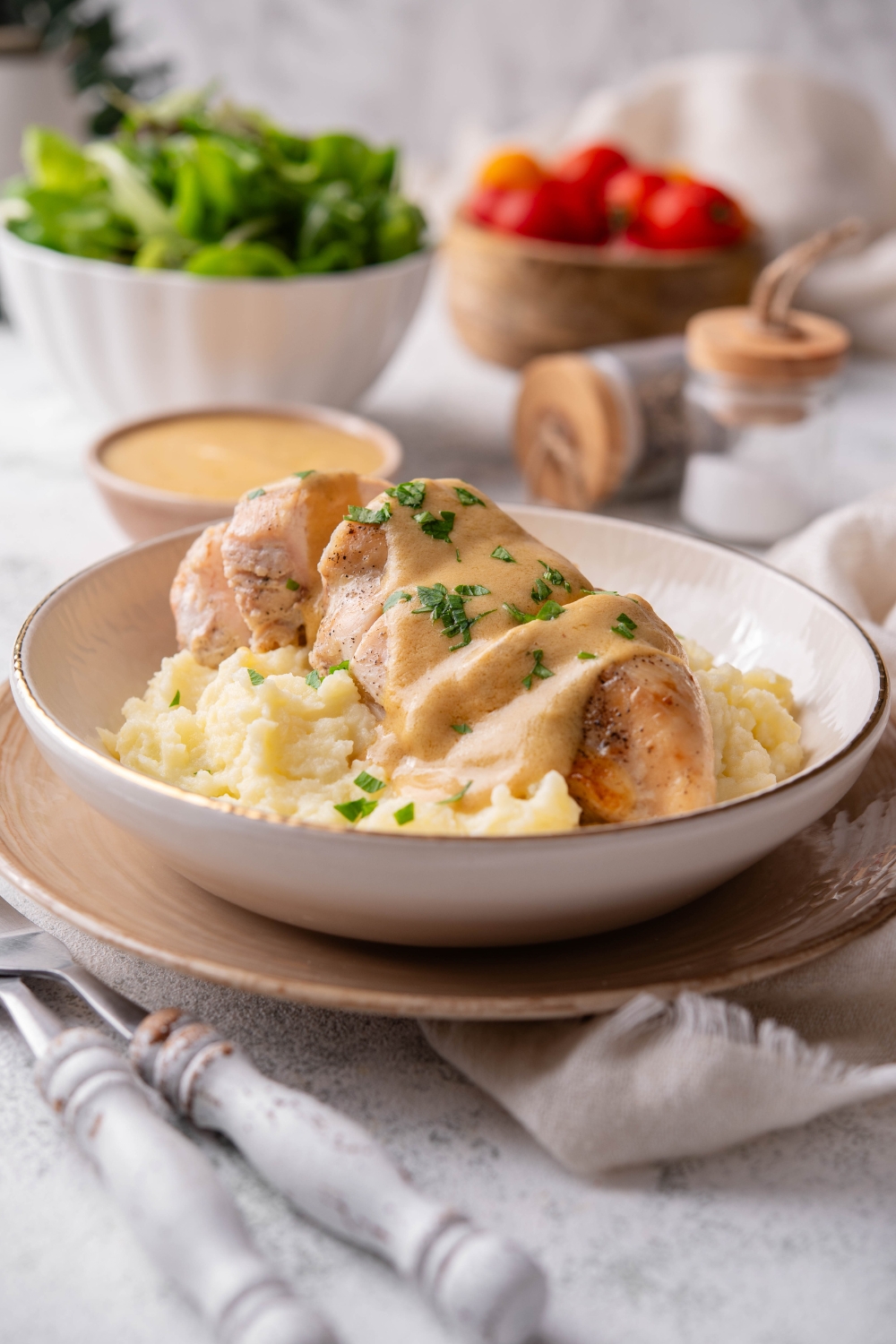 A plate of cooked and sliced chicken breast covered in a creamy brown sauce, garnished with fresh herbs, on a bed of mashed potatoes.