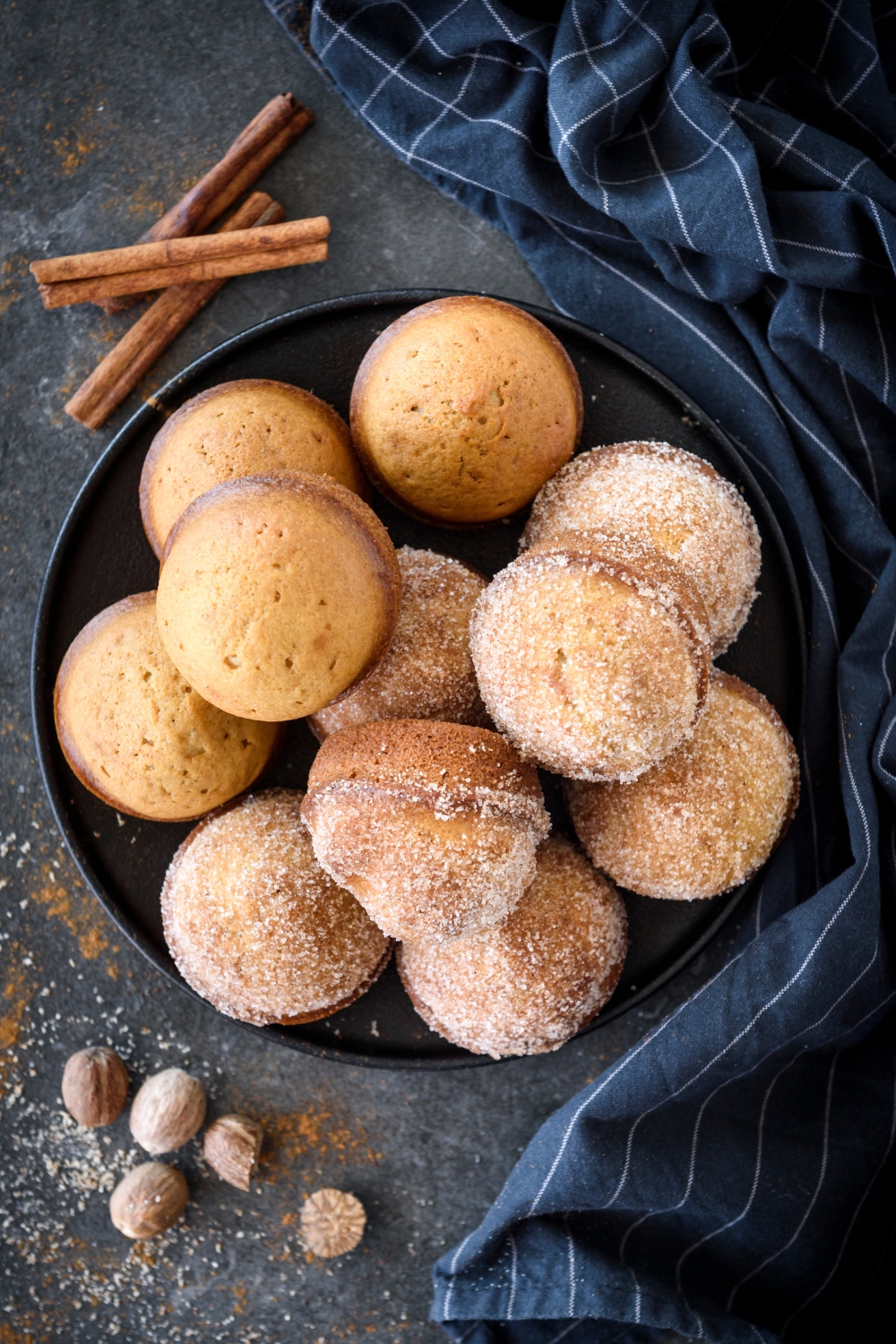 A pile of muffins on a black plate with half covered in cinnamon sugar.