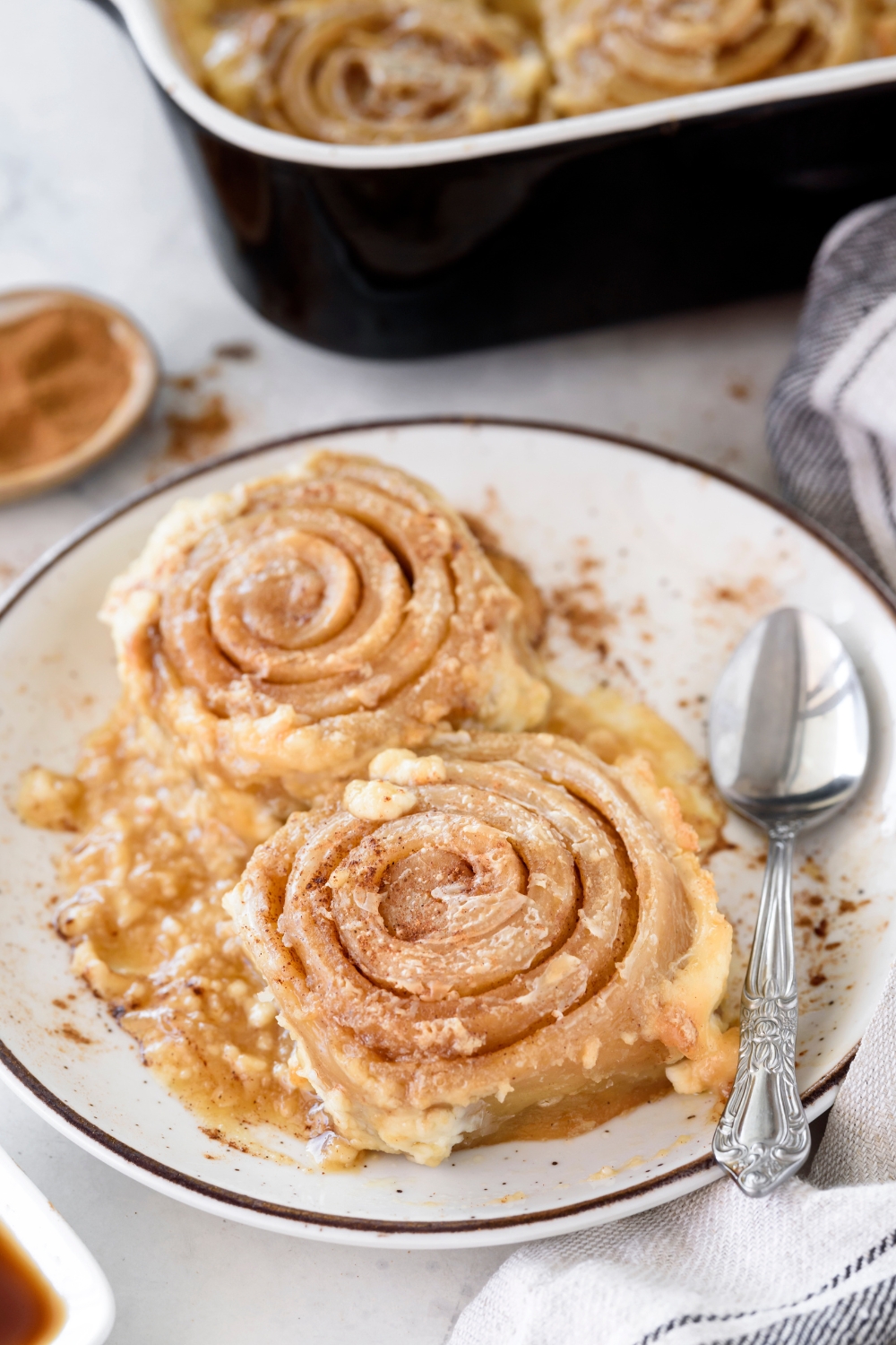 Two cinnamon rolls covered in a brown sugar butter mixture and dusted with cinnamon.