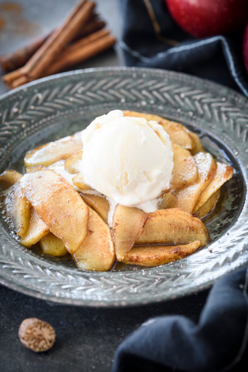 A blue bowl filled with baked apple slices coated in cinnamon topped with melting vanilla ice cream.