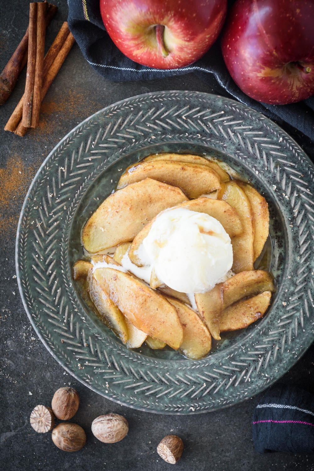 Overhead view of a blue bowl filled with baked apple slices coated in cinnamon topped with melting vanilla ice cream.