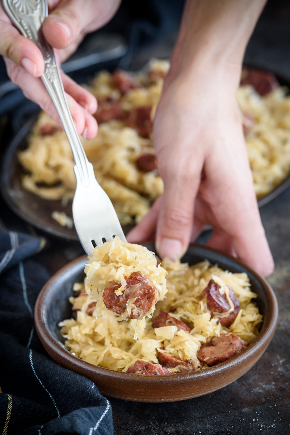 A fork holding sauerkraut and a sausage slice above a bowl of sauerkraut and sausages.