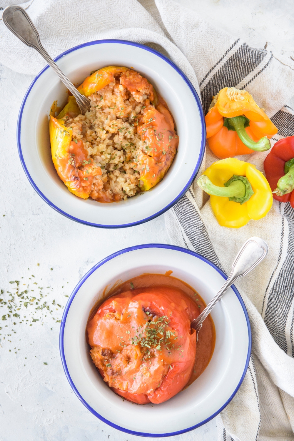 Two bowls of stuffed bell peppers covered stuffed with rice and ground meat and covered in tomato sauce.