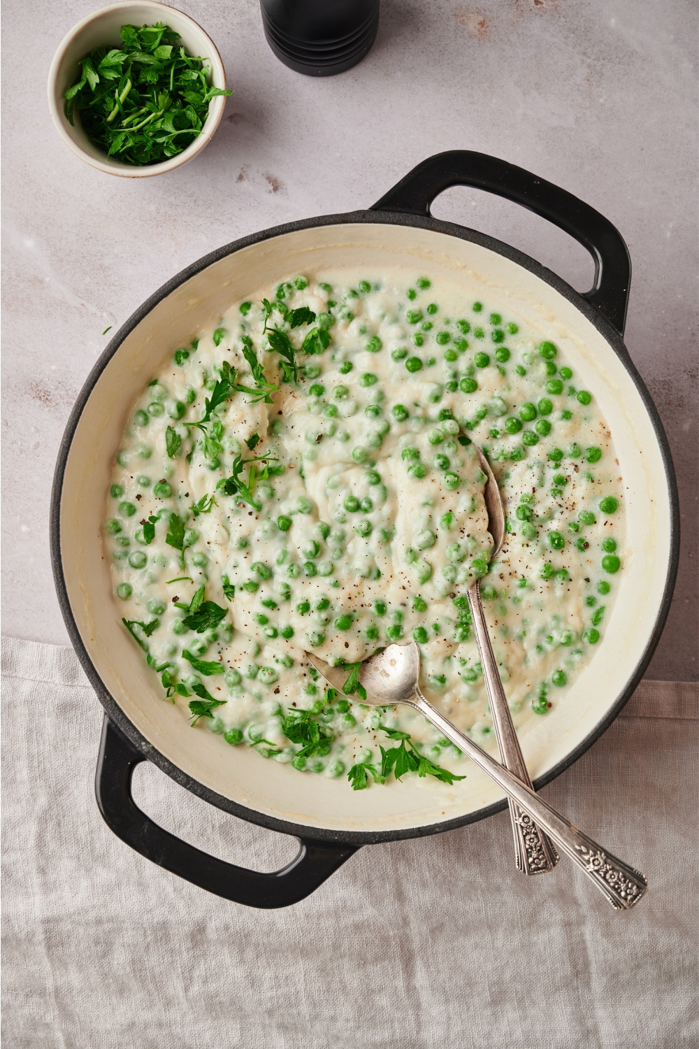 Creamed peas in a skillet with a set of serving spoons in it.